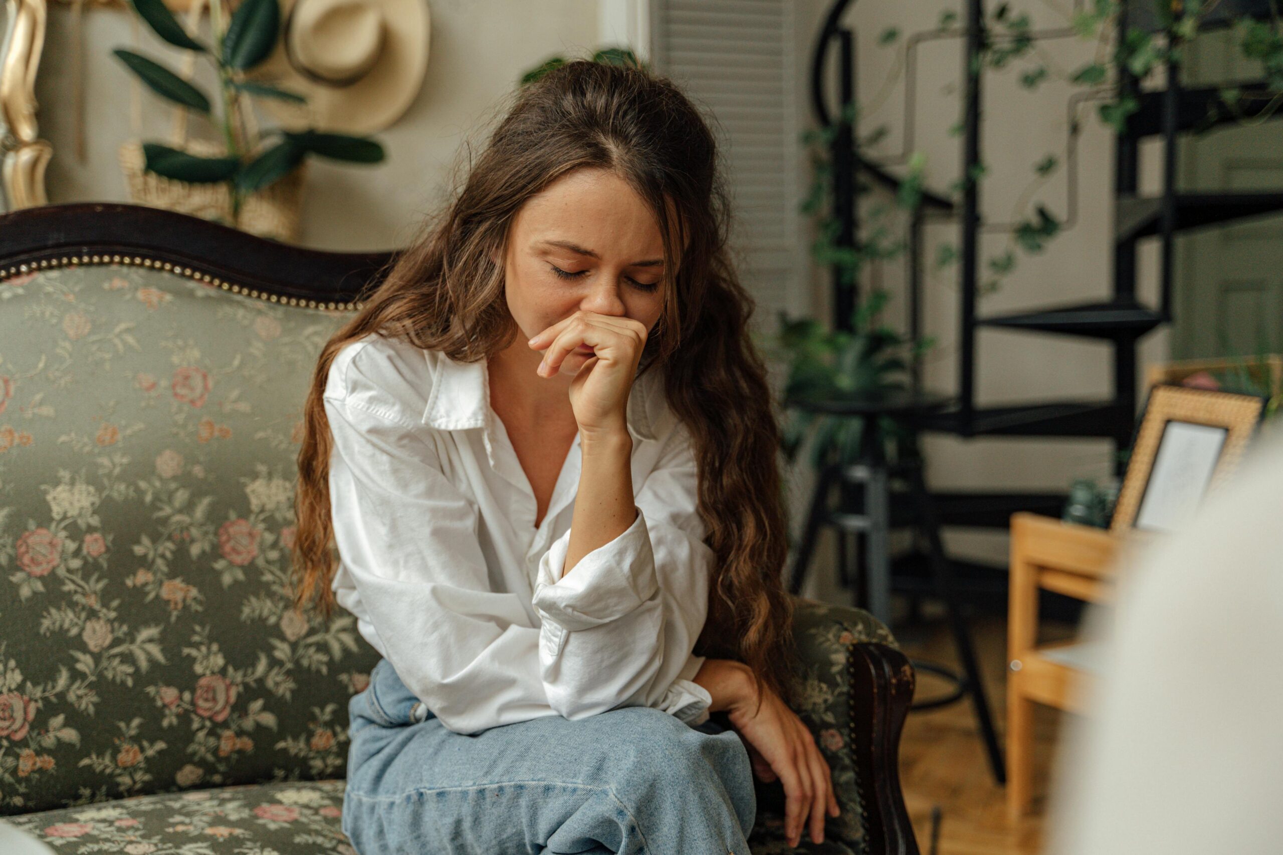 Home Woman in a white shirt sitting thoughtfully on a vintage sofa indoors.