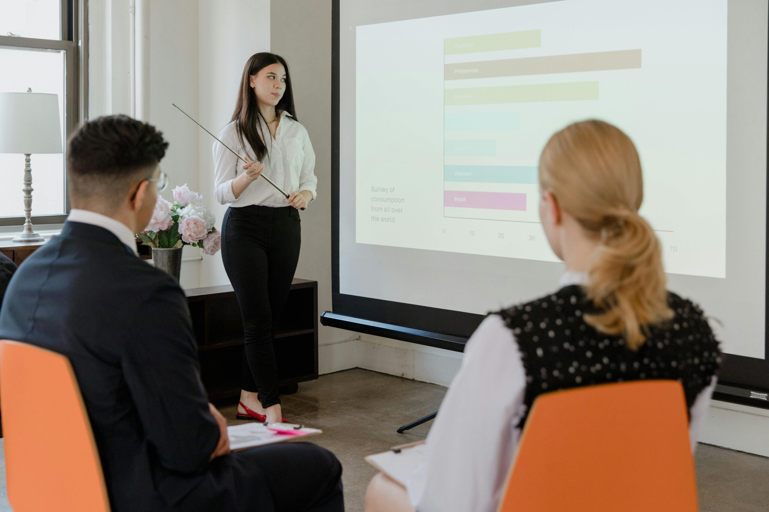 Services A young professional presenting data in a modern office to attentive colleagues.